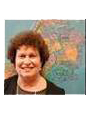 Smiling, middle-aged white woman with short, brown curly hair in front of a wall map of New York City
